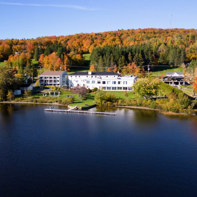 Le Manoir Lac-Etchemin au bord du lac avec les arbres aux couleurs automnales derrière.