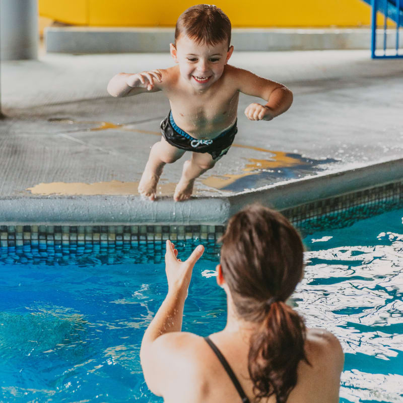 Mother in the hotel pool catching her son jumping in the water.