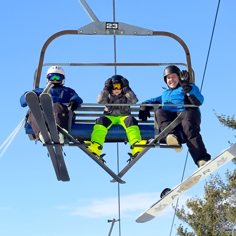 Father and two sons on a ski lift smiling at the camera.
