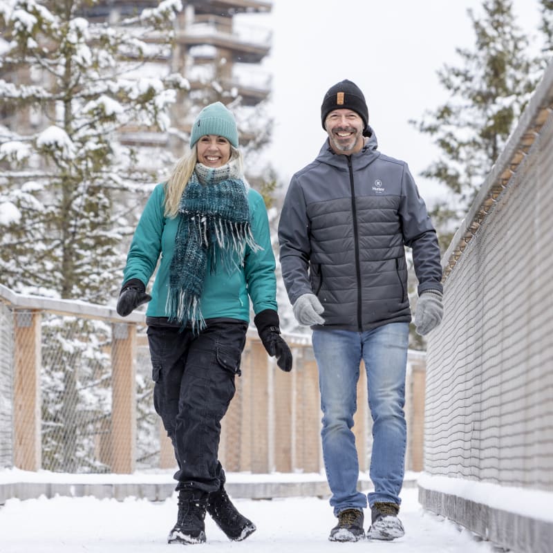 Couple souriant sur une promenage en bois enneigée.