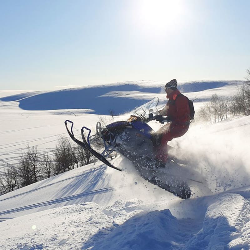 Person snowmobiling through a vast snow-covered landscape.