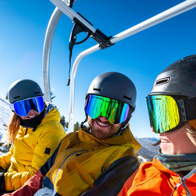 Three skiers in a lift, it's a sunny day and they're smiling.