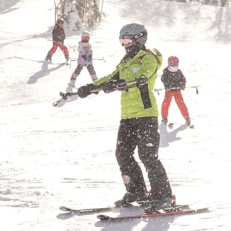 Moniteur de ski avec apprentis skieurs et skieuses derrière lui.