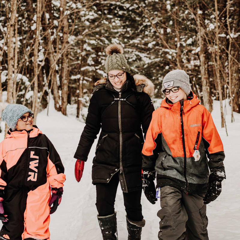 Une mère et deux enfants, tous souriants, dans une forêt enneigée.