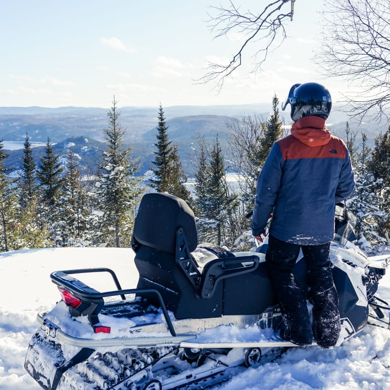 Snowmobiler looking out at the forest and river.