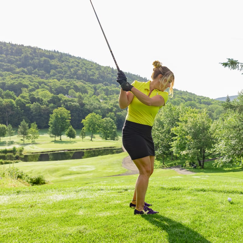 Woman on a golf course about to hit the ball.