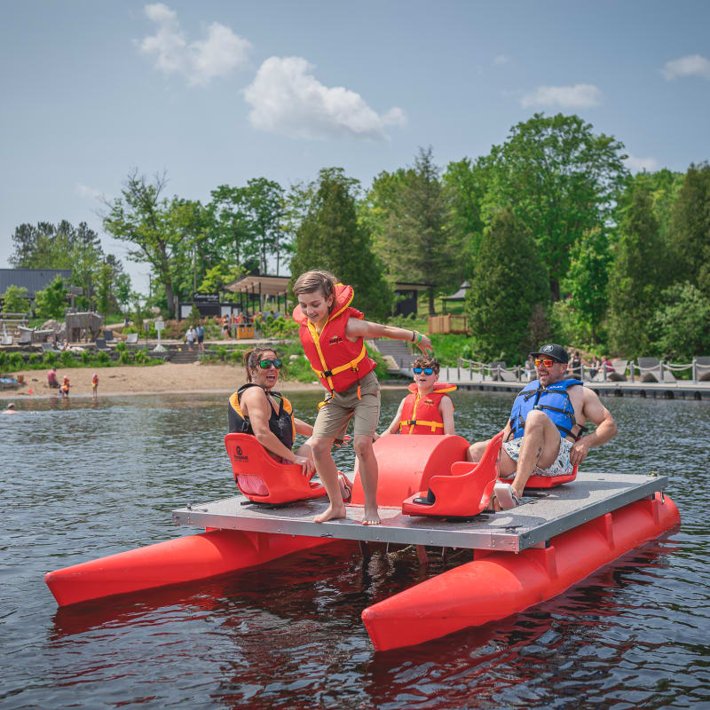 Family of four on a big pedal boat; a boy is about to jump into the lake.
