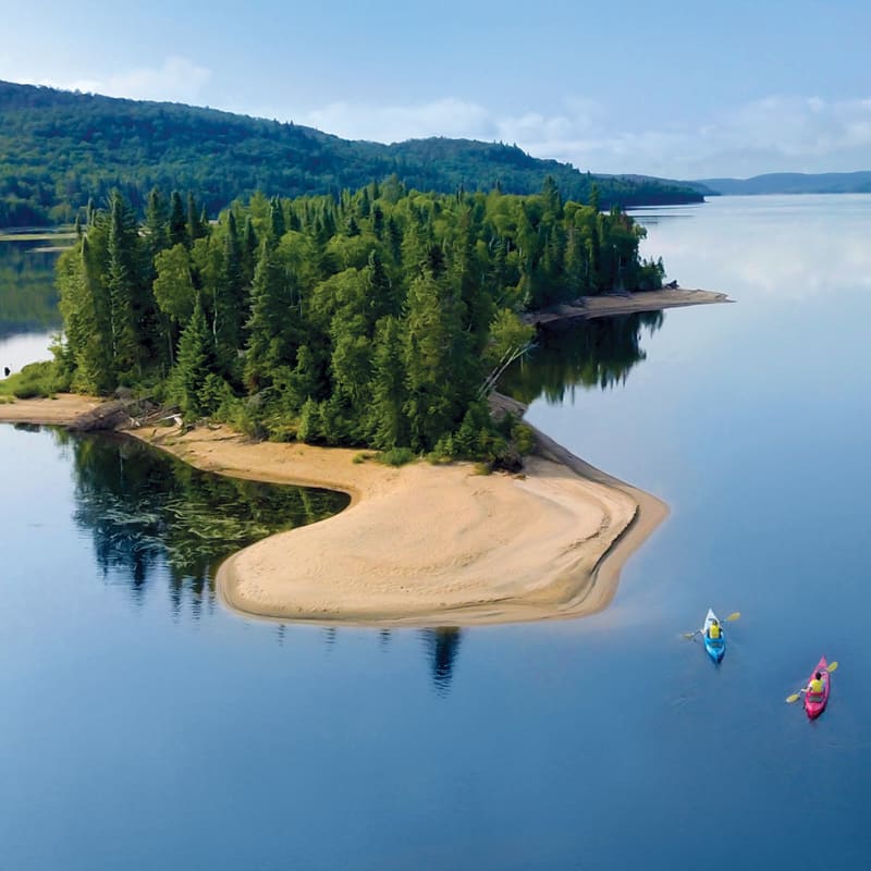 Vue aérienne d’une petite île avec plage au milieu d’un grand lac.
