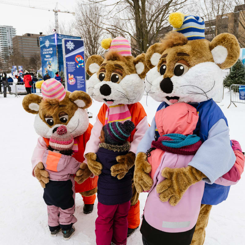 Three mascots outside in the winter giving kids hugs.