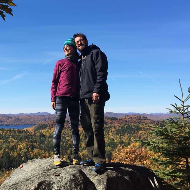 Two people posing on a rock in front of a fall landscape.