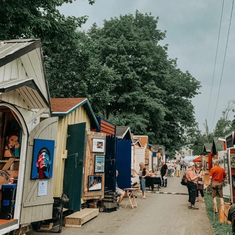 An alleyway lined with small cabins showcasing works of art.