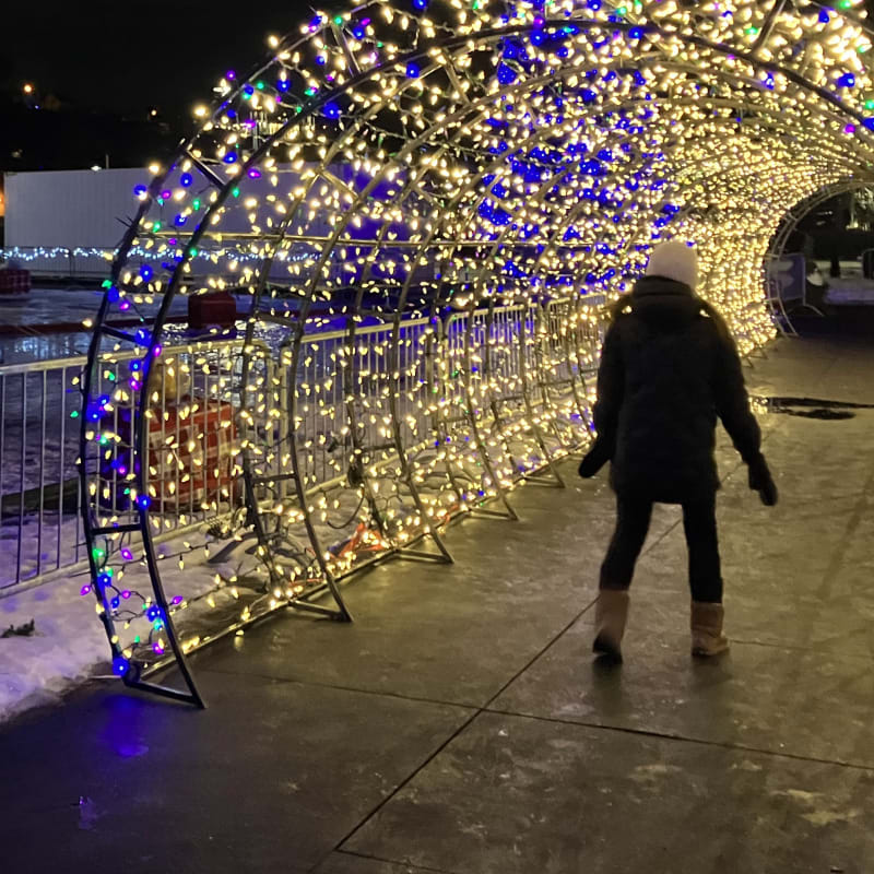 Woman walking under an illuminated arch outside.