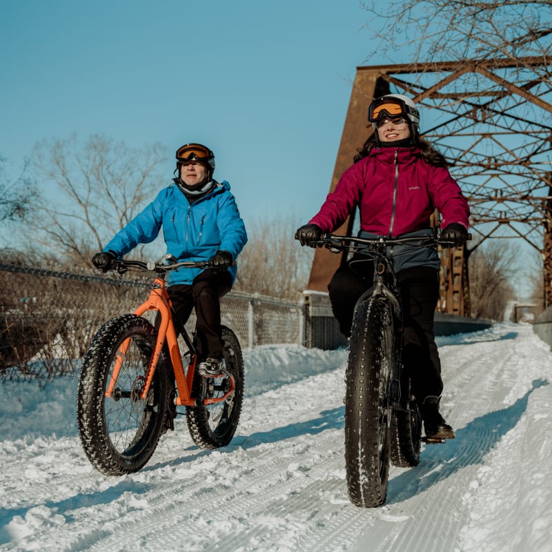 Two people on fatbikes on a snow-covered trail.