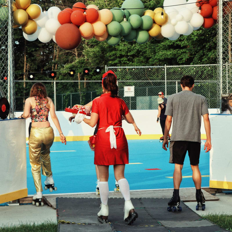 Three people on roller skates preparing to enter a rink decorated with balloons.