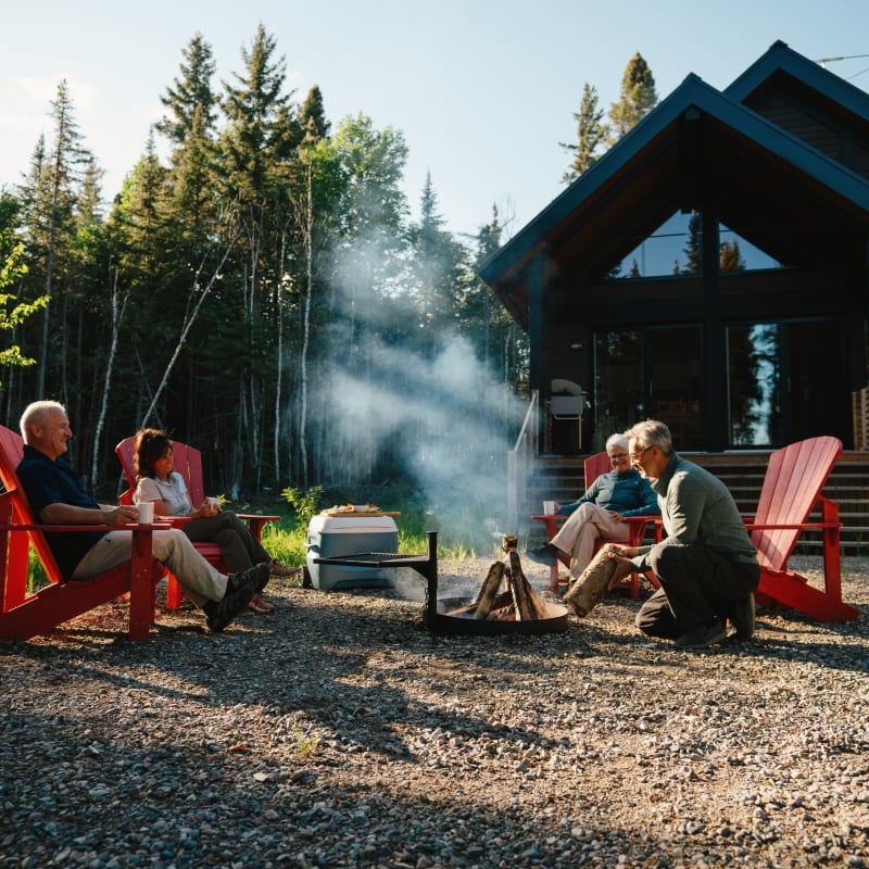 Four people sitting in Adirondack chairs around a field fire in front of a Horizon cabin.