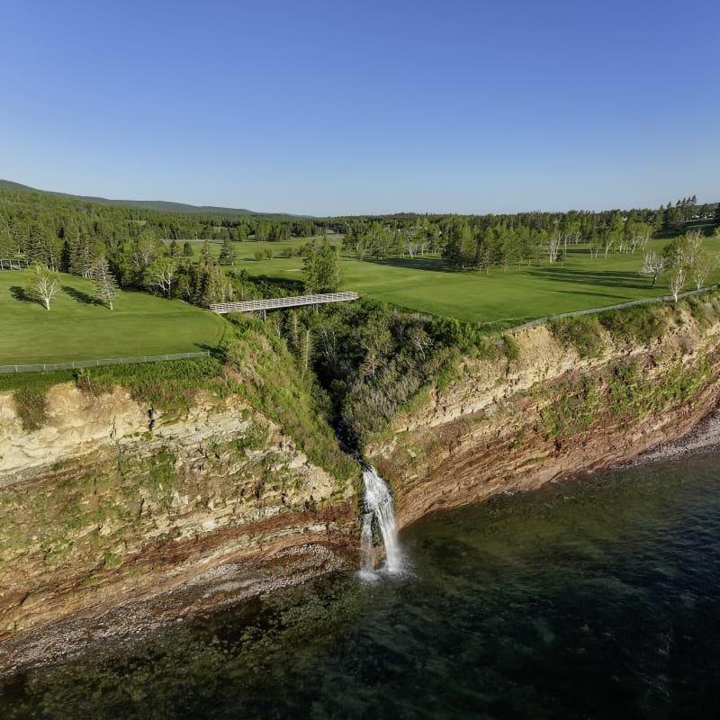 At the edge of a lush green golf course, a body of water meets a reddish cliff. 