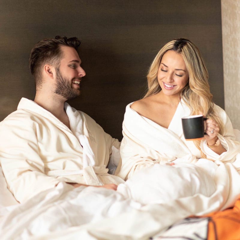 Couple relaxing in bed wearing bathrobes and enjoying a cup of coffee.