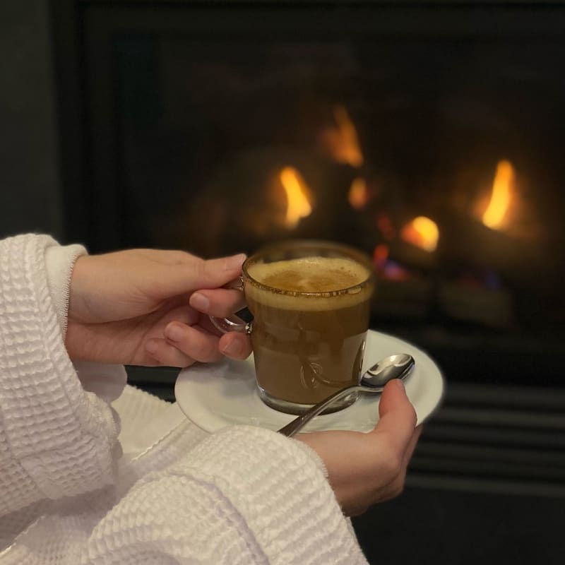 Woman in a bathrobe holding a coffee in front of the fireplace.