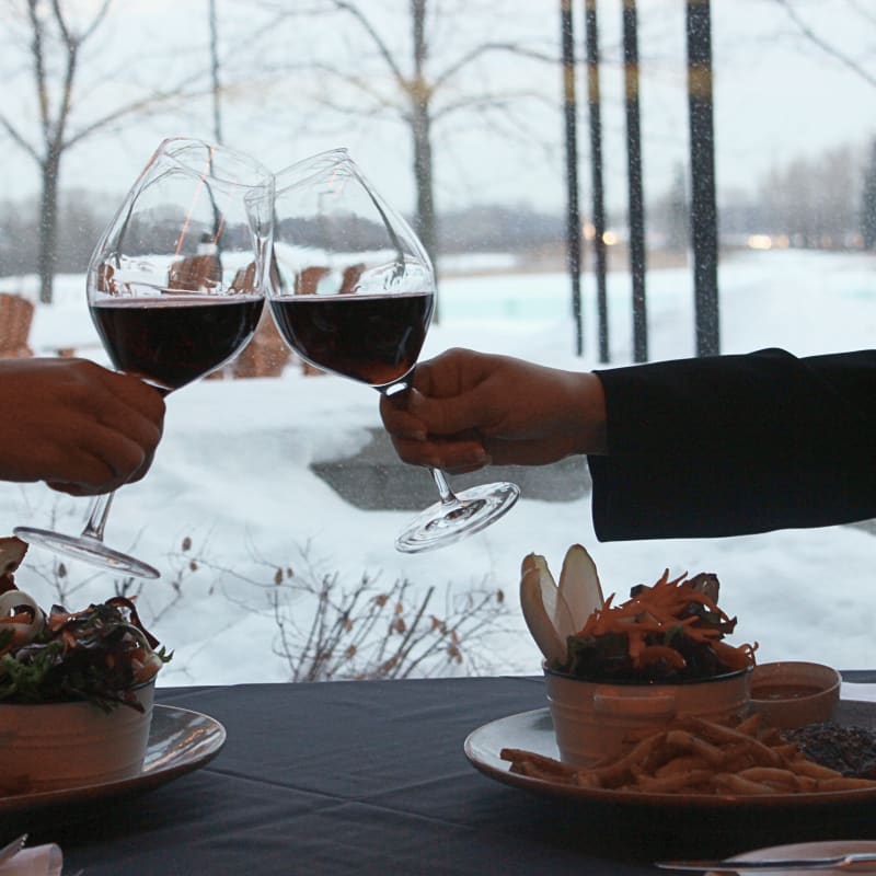 Two people clinking their glasses in front of a window in a restaurant in the winter.