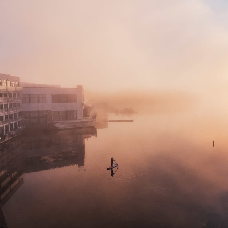 Aerial view of a woman stand-up paddleboarding on the lake at dawn.