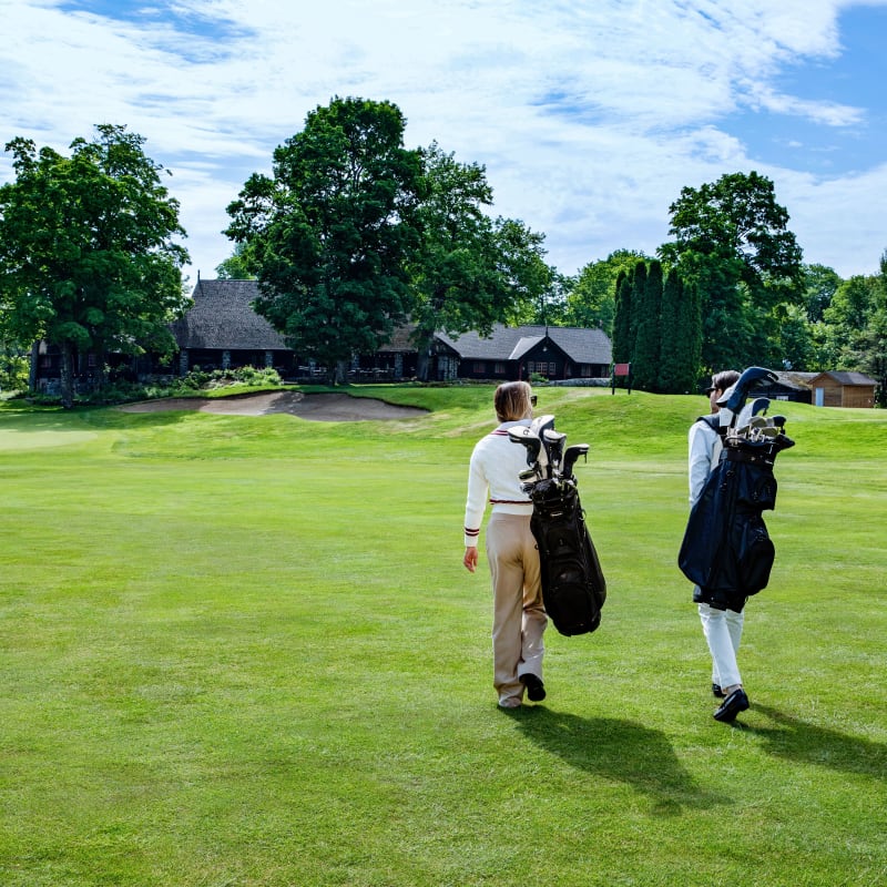 Deux personnes sur un terrain de golf qui portent leur sac sur le dos.