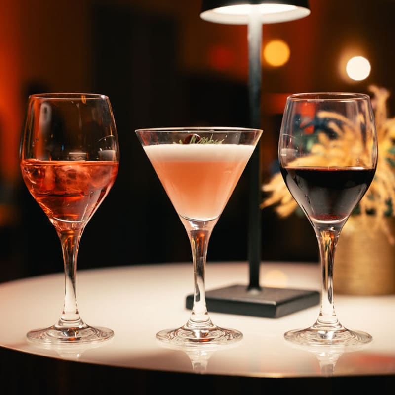 Deux verres à vin et un verre à martini alignés sur une table sous une lumière tamisée.