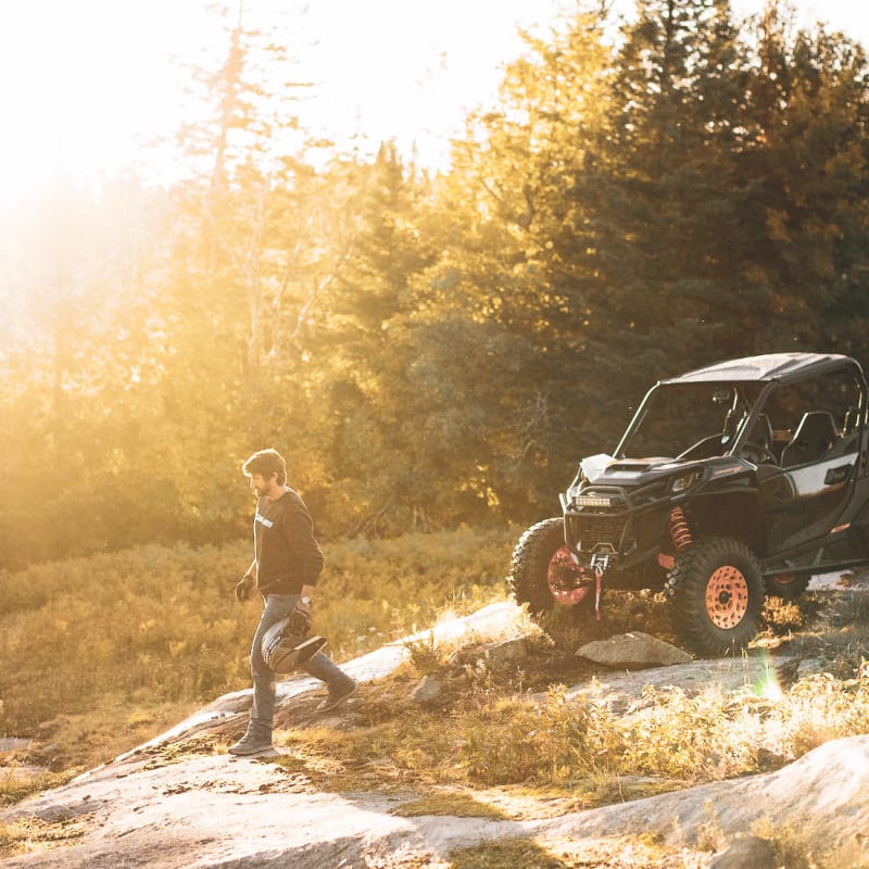 A person standing next to an ATV in nature, with the sun shining brightly.