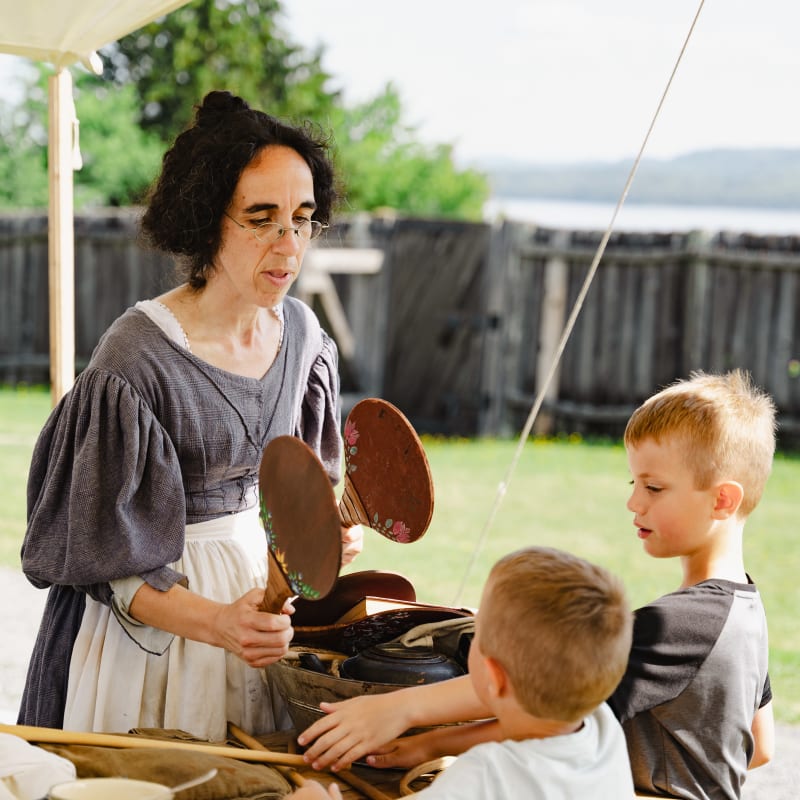 A woman in period costume interacting with two young boys.