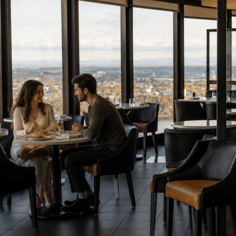 Un homme et une femme attablés en tête-à-tête à un restaurant en journée, avec une vue sur Québec de haut.