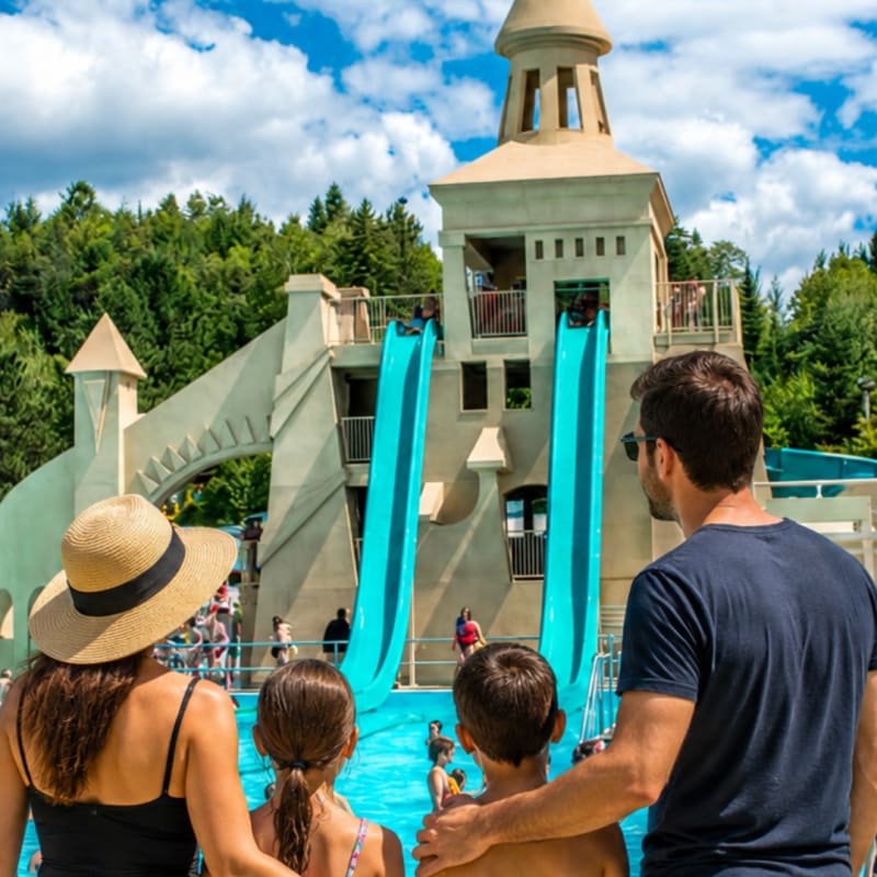 Une mère et un père avec leurs deux enfants; ils sont de dos à la caméra et regardent un château avec glissades d'eau devant eux. 