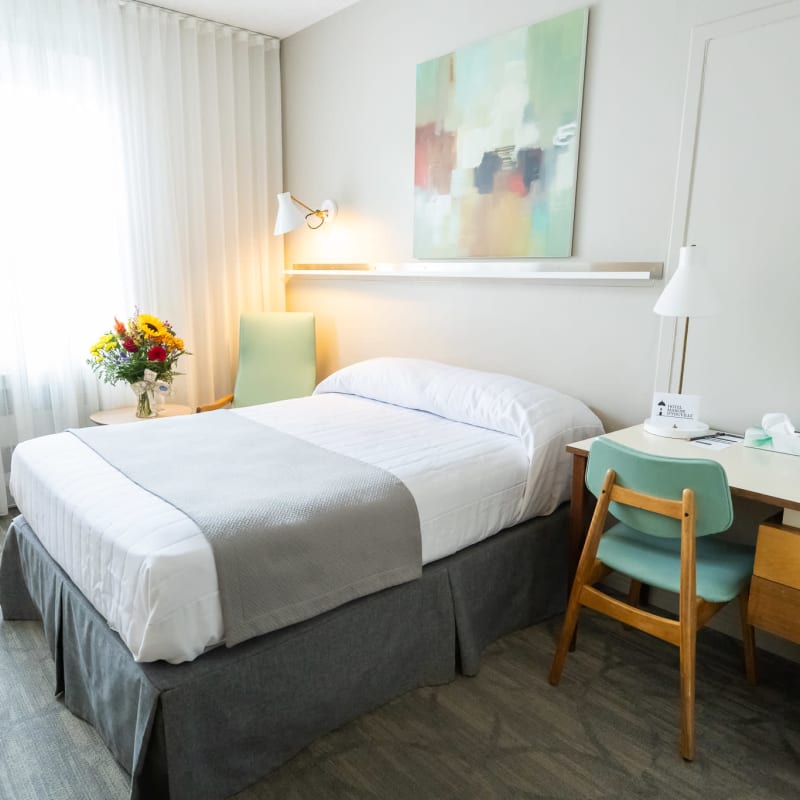 Chambre lumineuse de l'Hôtel Manoir d'Youville avec lit et bureau de travail.