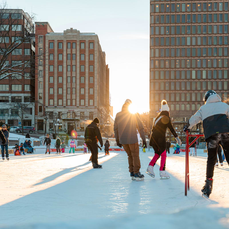 Several people on the ice rink at Place d'Youville as the sun sets on the horizon.
