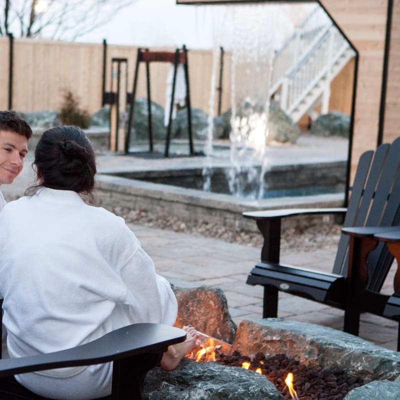 2 people relaxing by a fire outside at the spa.