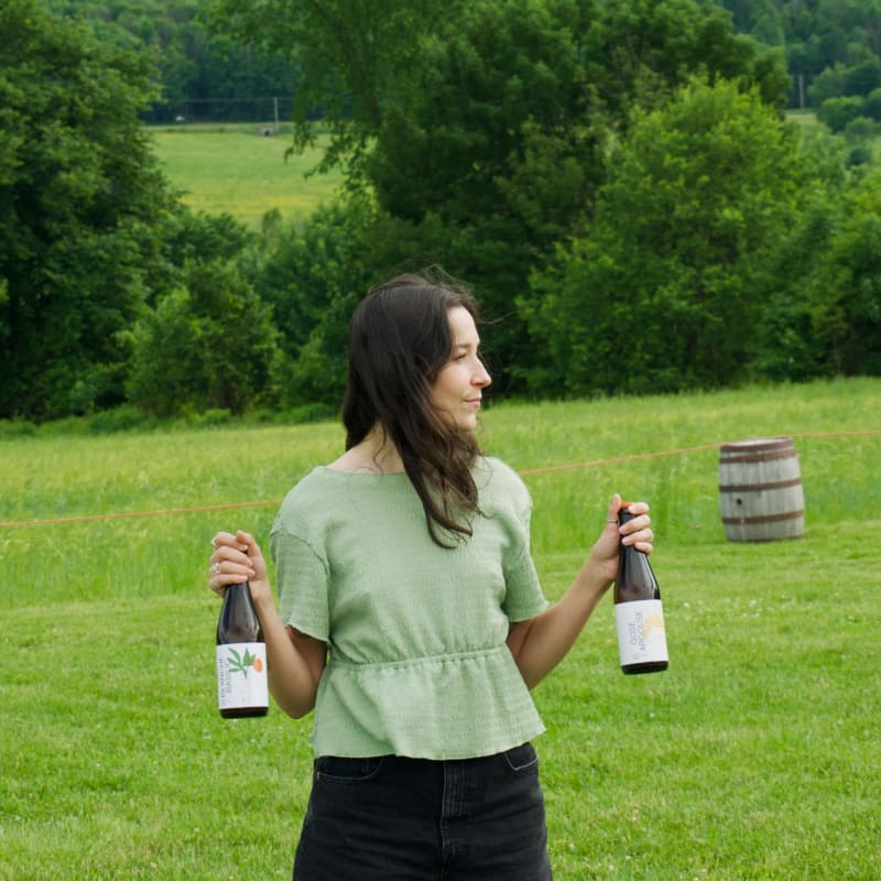Femme dans un champ qui tient deux bouteilles de vin.