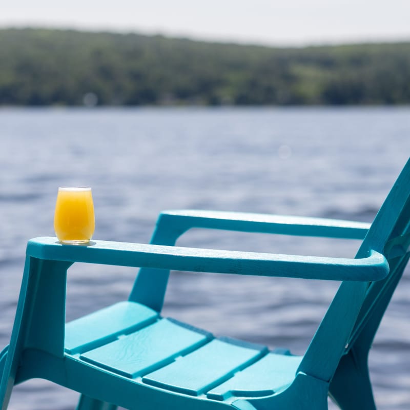 Chaise Adirondack turquoise au bord de l'eau; un cocktail est posé sur l'accoudoir.