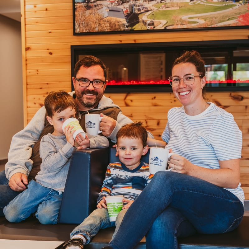 Deux parents et deux enfants souriants, tasse à la main, devant un mur en bois naturel.