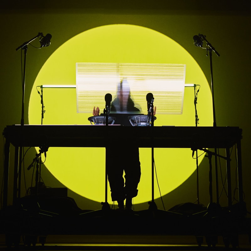 DJ sur une scène, derrière sa table tournante avec un fond lumineux rond jaune soleil