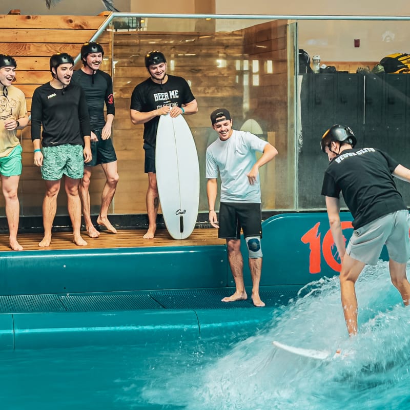 Man surfing in an indoor pool, with a group of people watching