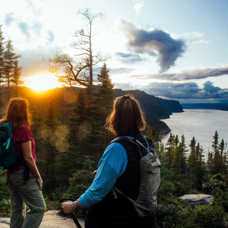 Parc national du Fjord-du-Saguenay - Two women on top of a mountain, forest and sunset in the background.