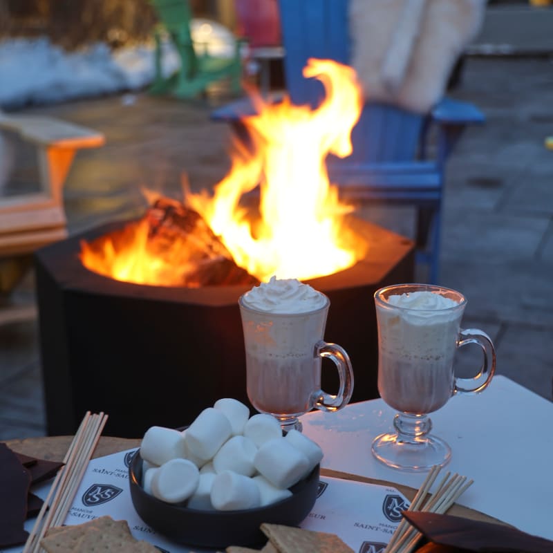 Outdoor firepit with two mugs of hot cocoa and ingredients to make s'mores.