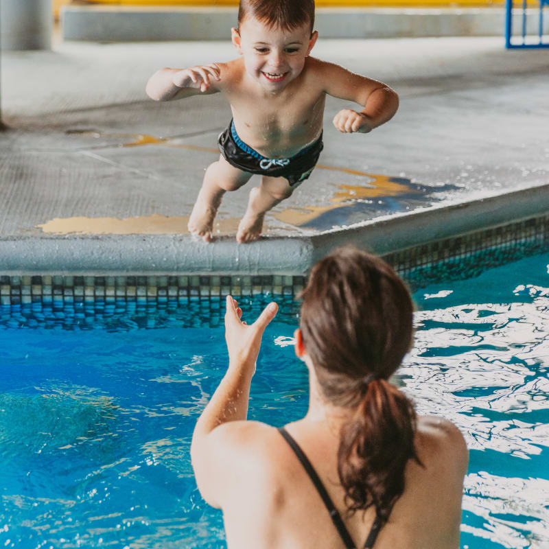 Mother in the hotel pool catching her son jumping in the water.