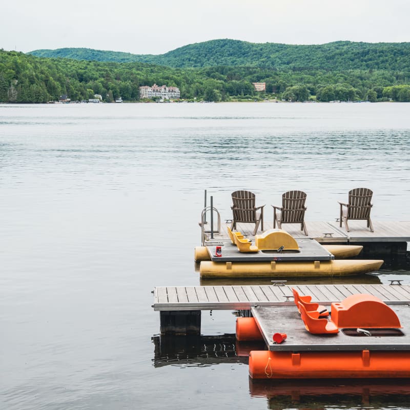 A dock, chairs, and a pedal boat by the lake.