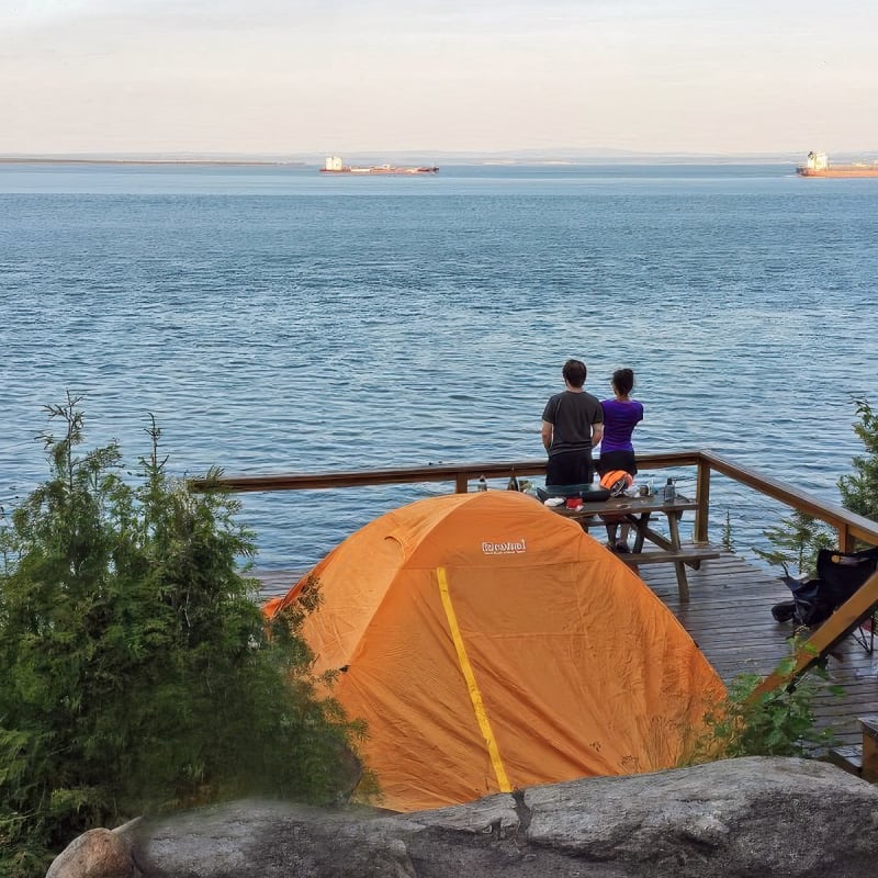 Couple à côté d'une tente qui regarde la mer.