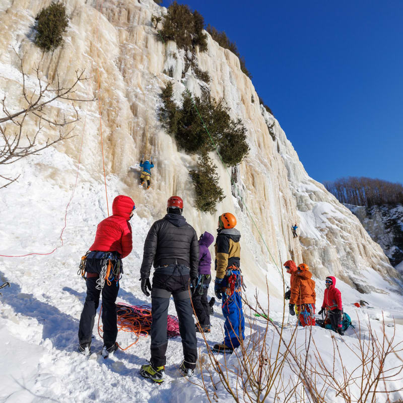 Spectators watch a person climbing an ice wall.