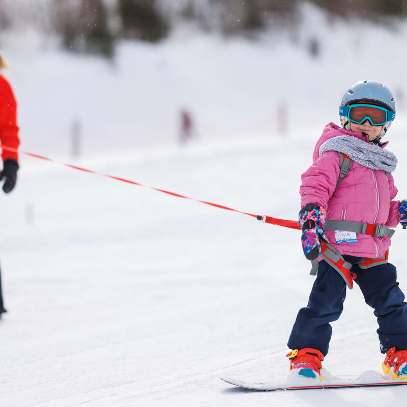 Young girl learning to snowboard with an instructor.