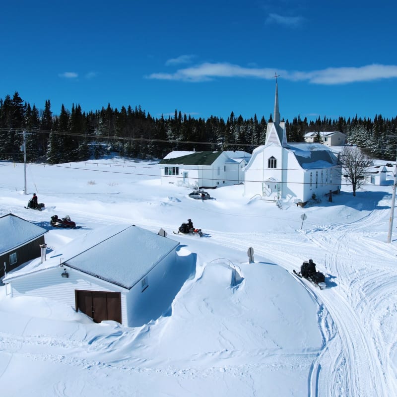 Groupe en motoneige dans un village enneigé.