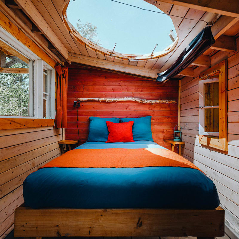 Canopée Lit - Intérieur d'une petite cabine avec lit et toit vitré.