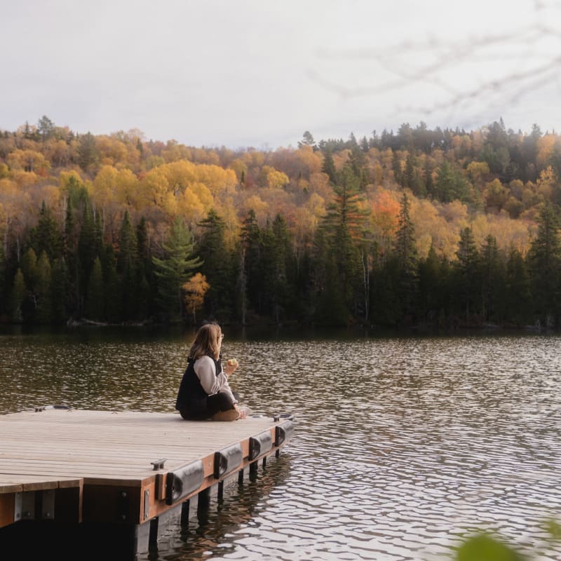 Femme assise sur un quai au bord d'un lac à l'automne.