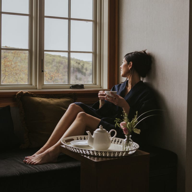Femme relaxant devant une fenêtre avec un thé.
