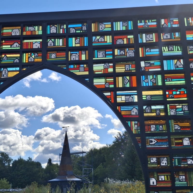 An outdoor art installation consisting of several stained-glass panels arranged to form a rural landscape.